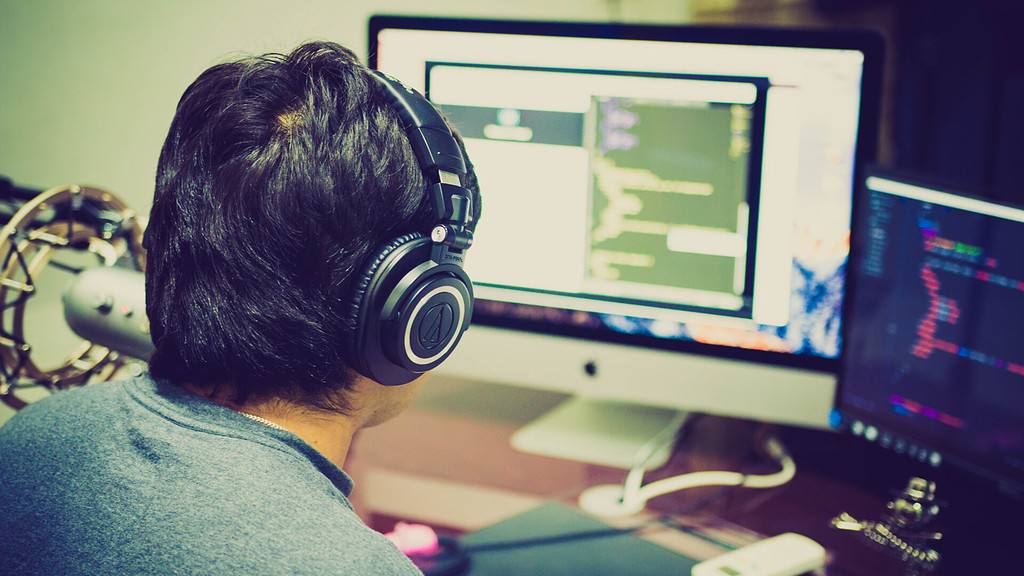 A man wearing headphones in front of a computer screen receiving IT support.