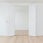 An empty room with a white door and wood floor.